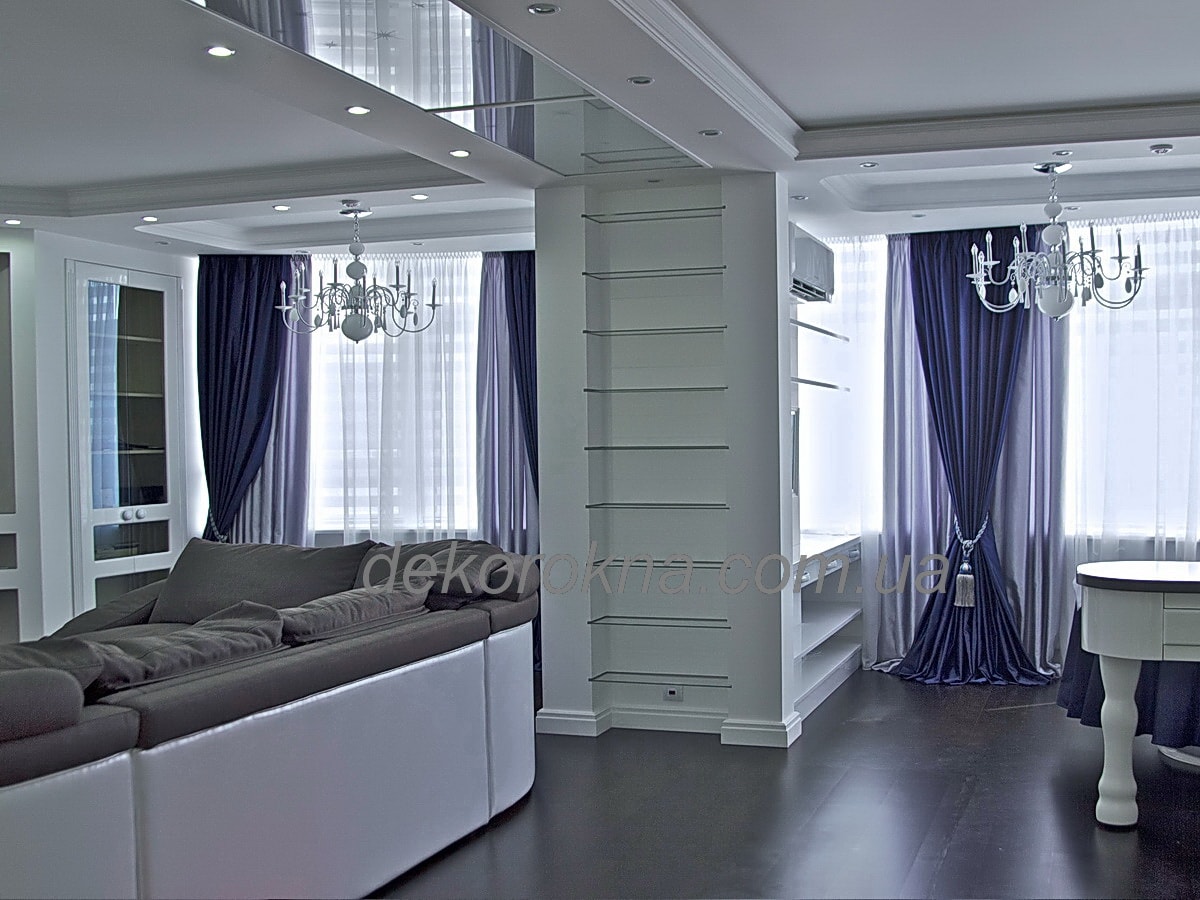 Синие декоротивные шторы в гостиной украшают кисти и дополняют серые рабочие шторы.