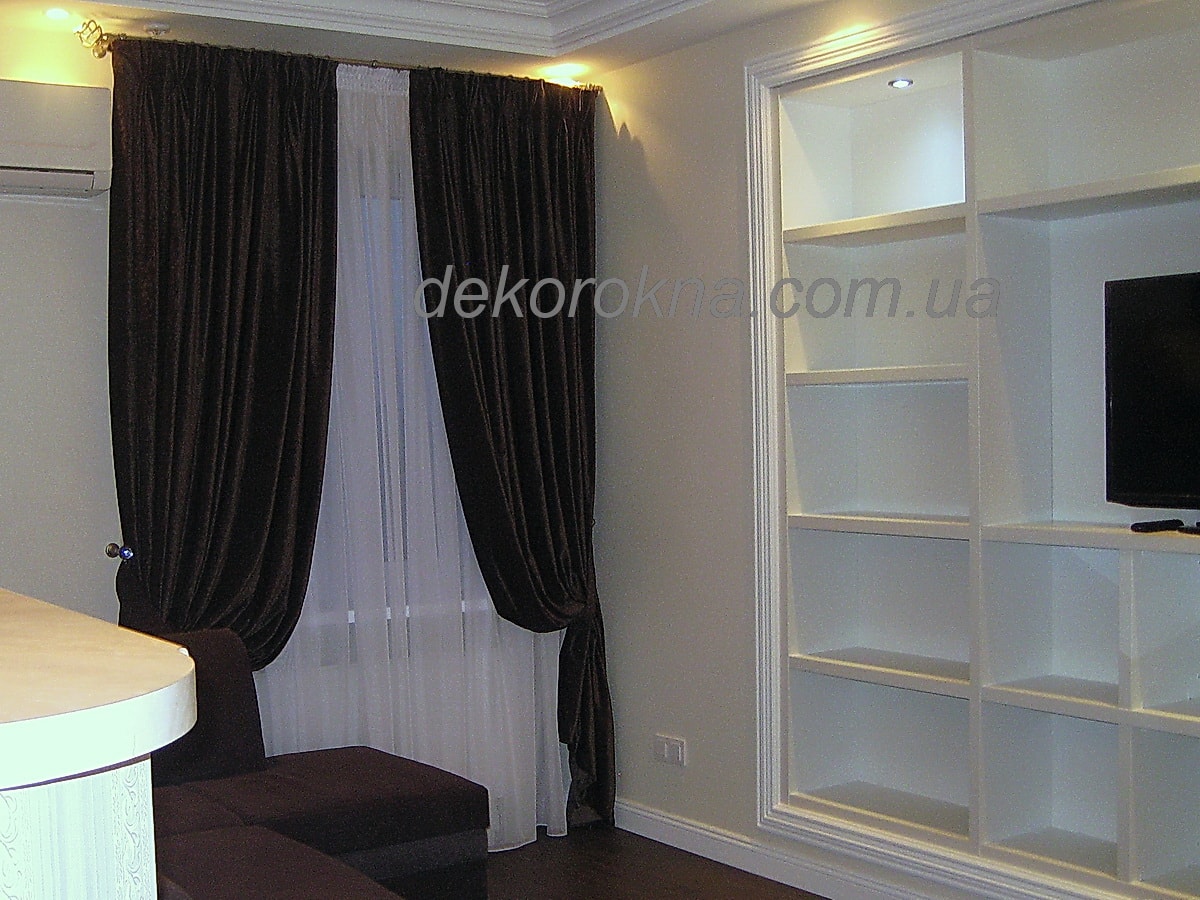 Темно-коричневые велюровые шторы в гостиной сочетаются с диваном. Трубчатый карниз установлен над оконным поемом.