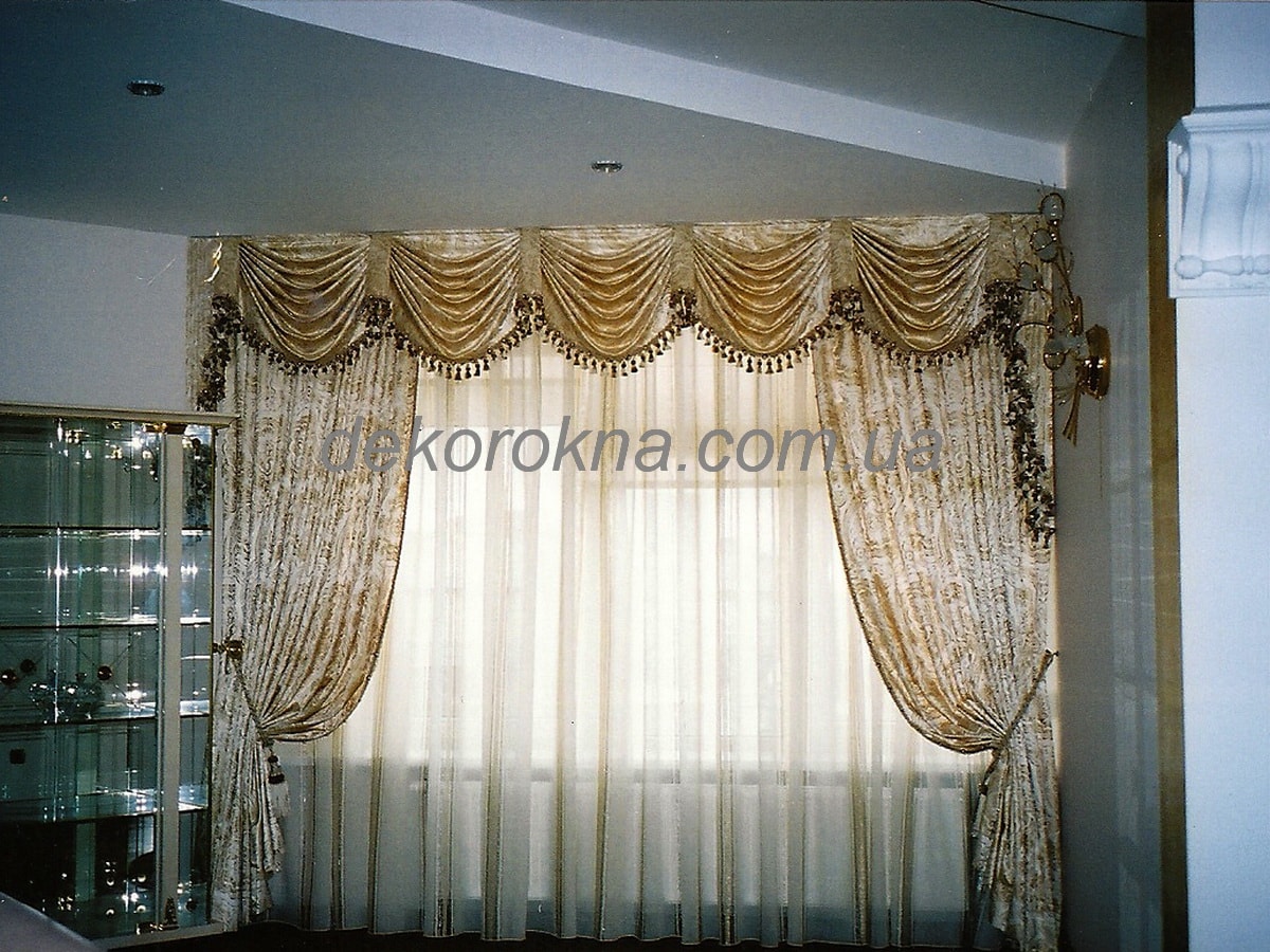 Классические шторы из мягкой беживо-золотой ткани. Ламбрекен с конническими складками украшен золотой отделочной тесьмой.